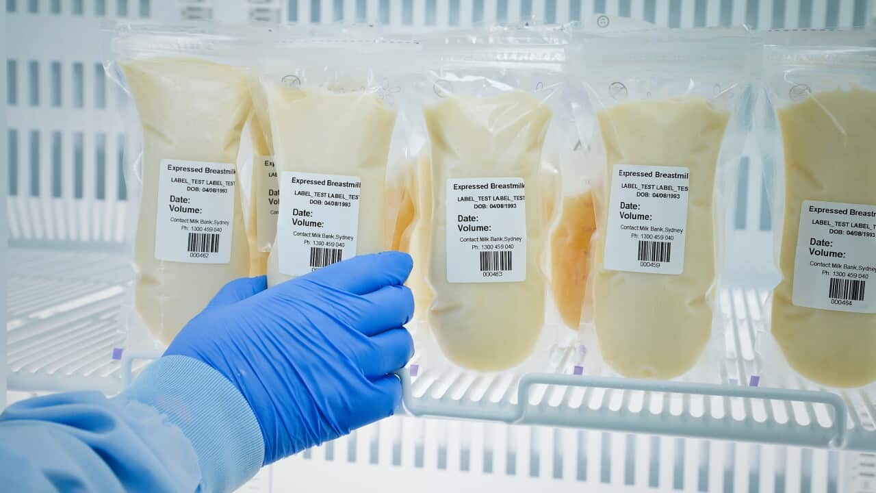 Someone reaching into a fridge and grabbing a package with a label that reads: "expressed breastmilk".