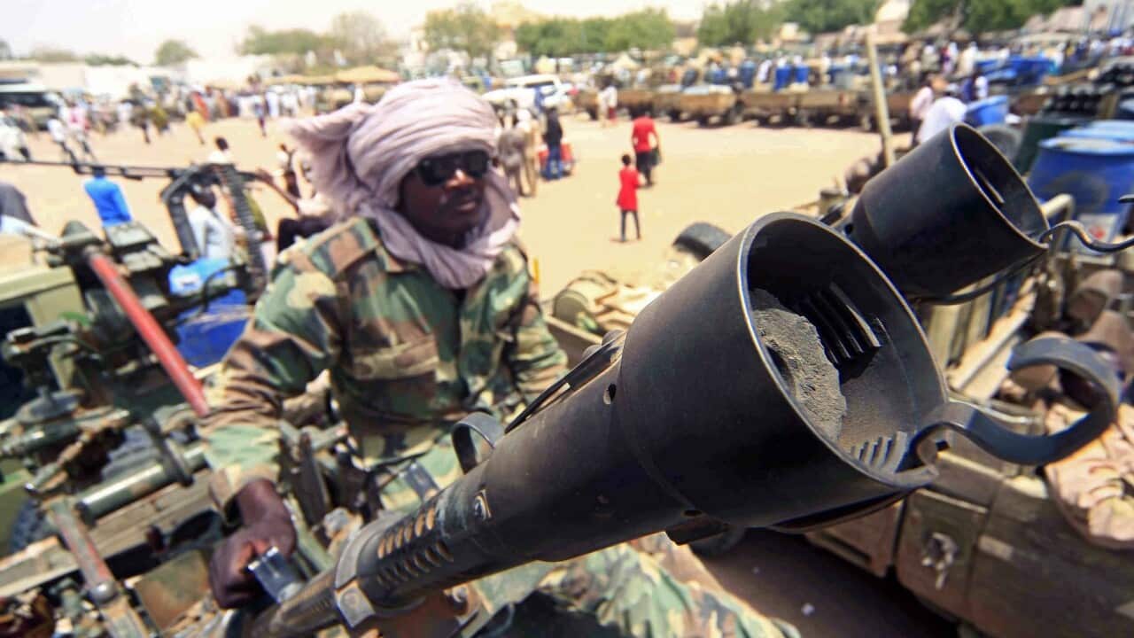 A militia members sits beside military equipment allegedly seized during a battle in Darfur