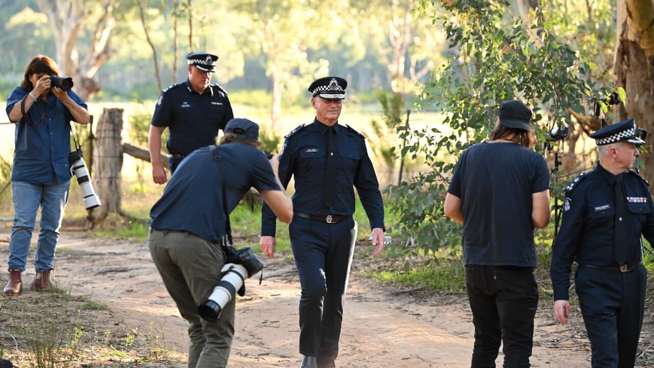 Chief Commissioner of Victoria Police Mike Bush departs after speaking to media at a press conference at the scene where fugitive Dezi Freeman was shot dead in Thologolong, Victoria. Bush is surroudned by press photographers and is dressed a dark blue police uniform and hat. He walks down a dirt track, dust kicking up around his ankles. On his face, he wears a wry smile.