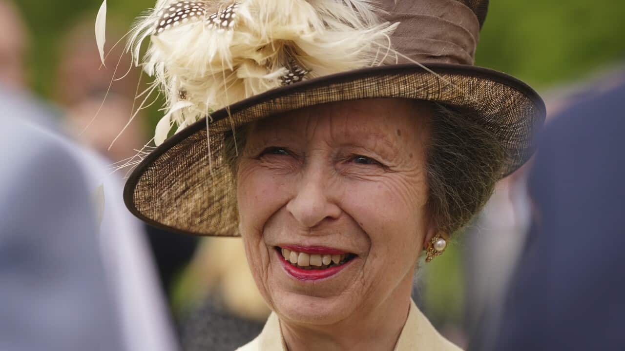 An older woman smiling in an elaborate beige hat