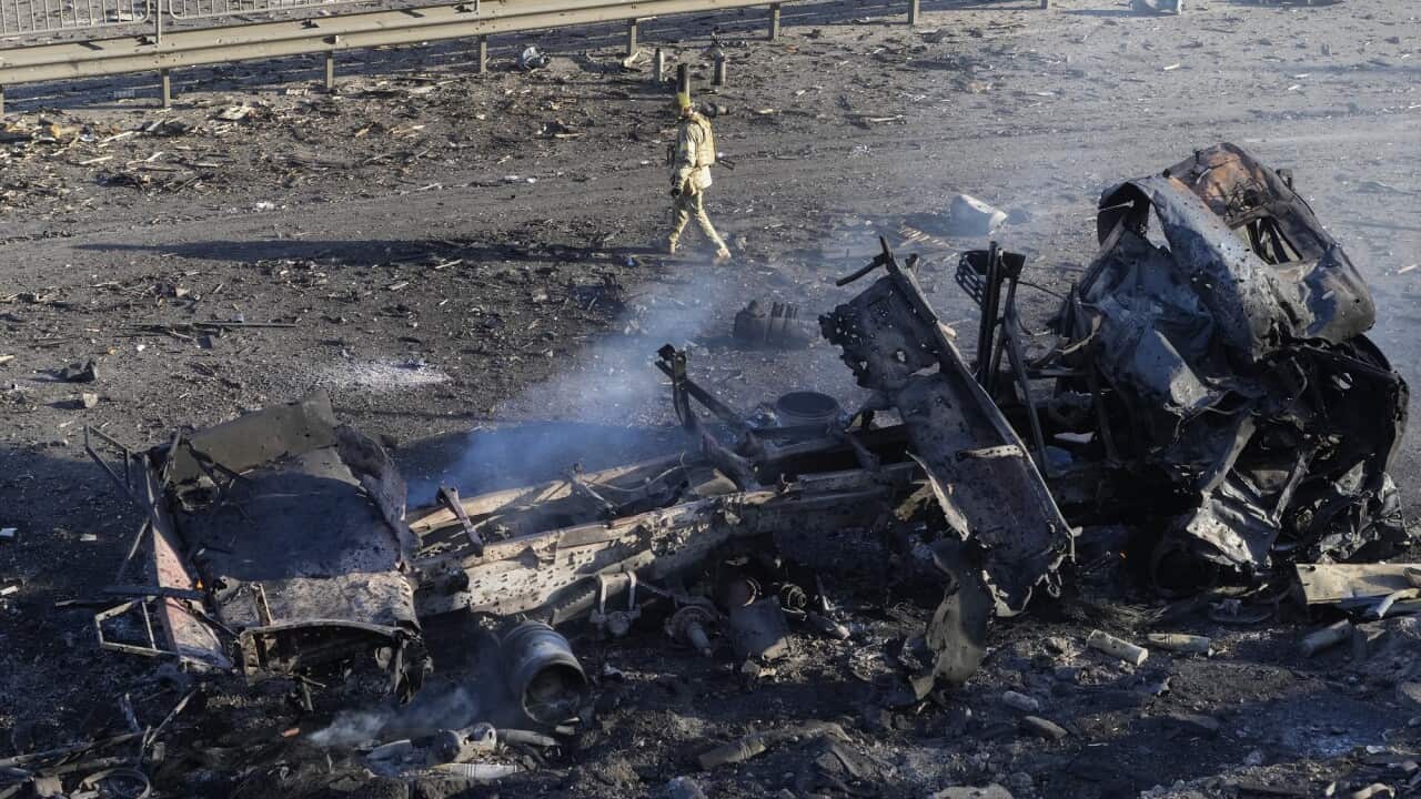 A real image of a soldier walking past debris of a burning truck on a street in Kyiv