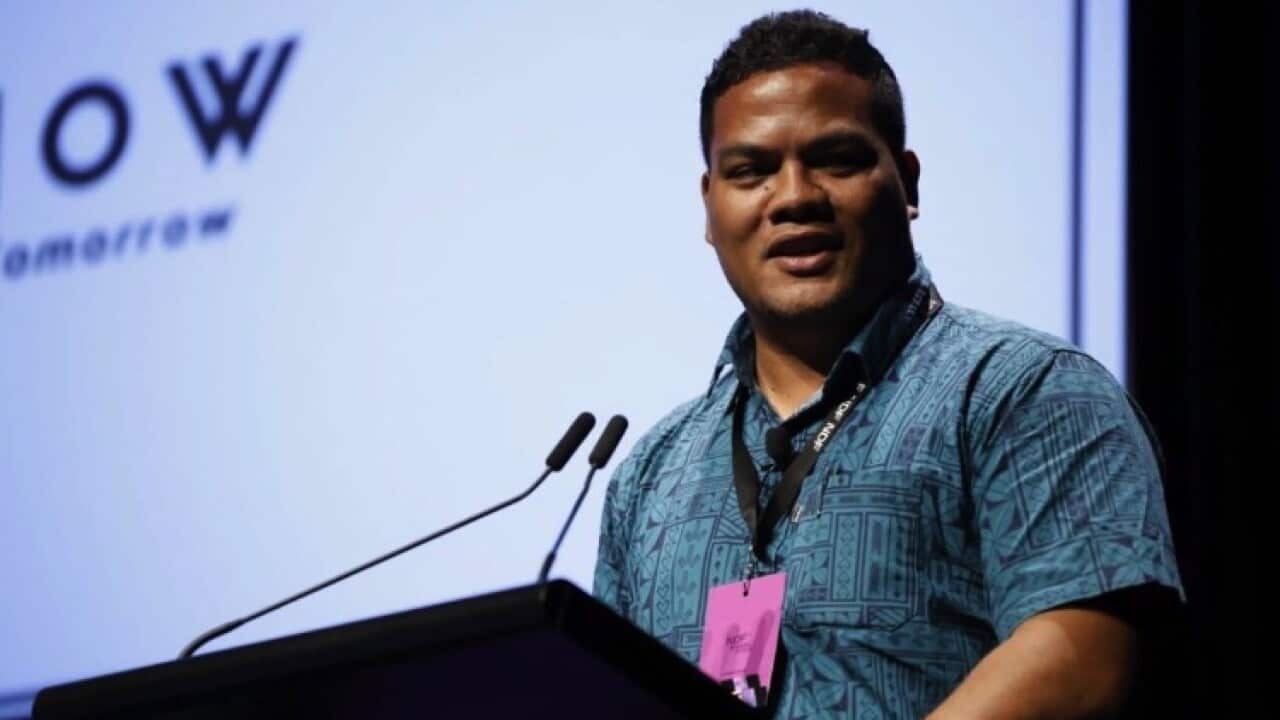 Simon Kofe wears a blue shirt as he speaks at a lectern.