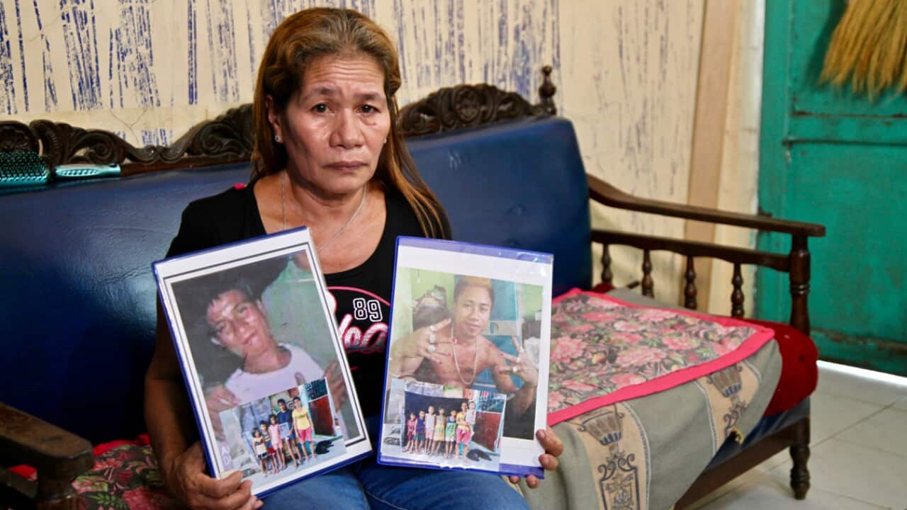 A woman sitting on a couch holding photographs of her sons