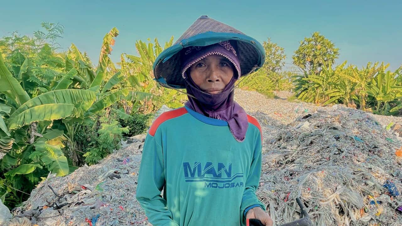 A woman stands in front of a large pile of shredded plastic waste.