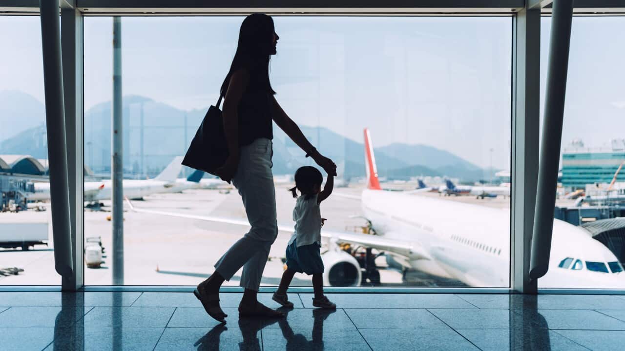 Silhouette of joyful young Asian mother holding hands of cute little daughter looking at airplane through window at the airport while waiting for departure