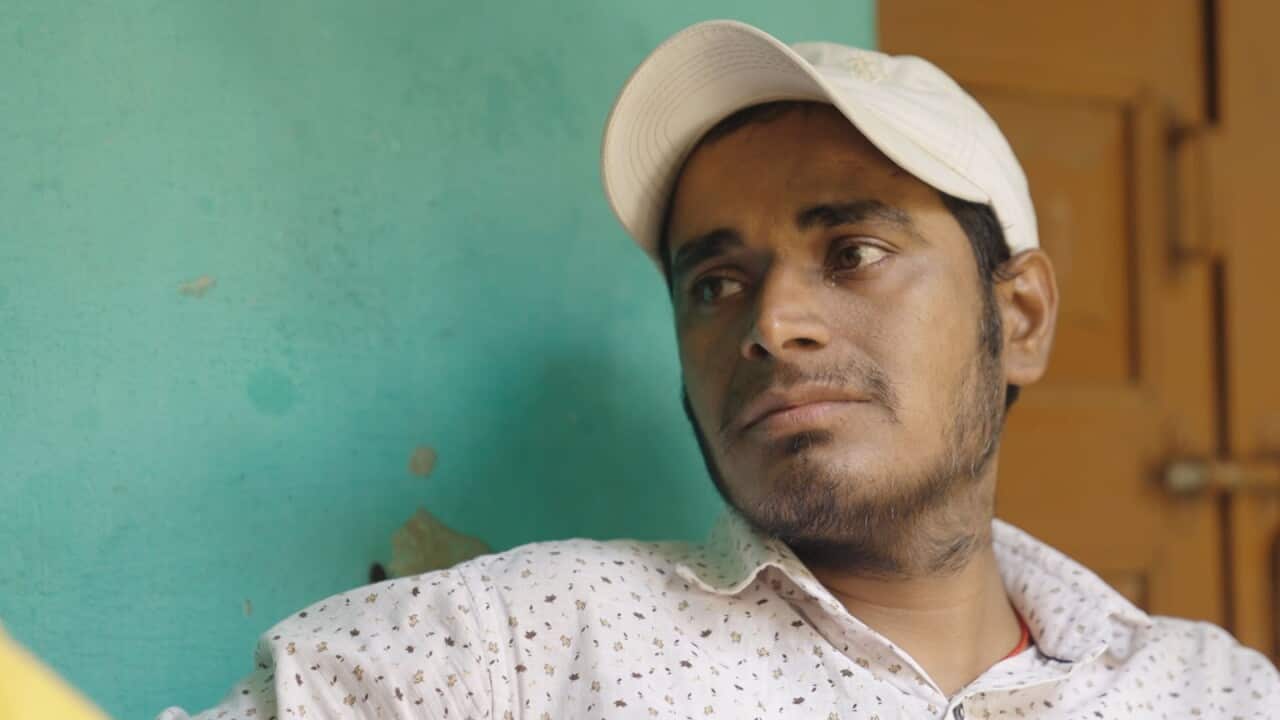 A young Indian man in a white shirt and a white baseball cap looking aside with tears in his eyes