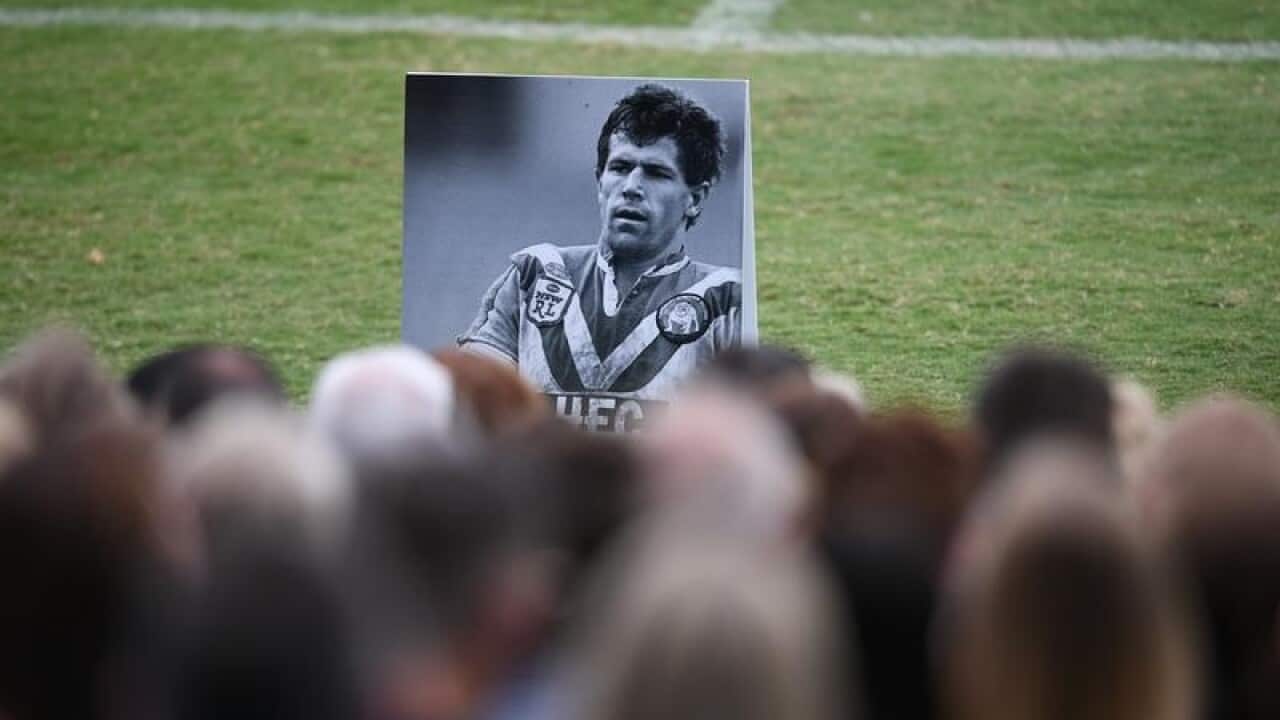 Mourners look at an image of Steve Folkes at Belmore Sports Ground.