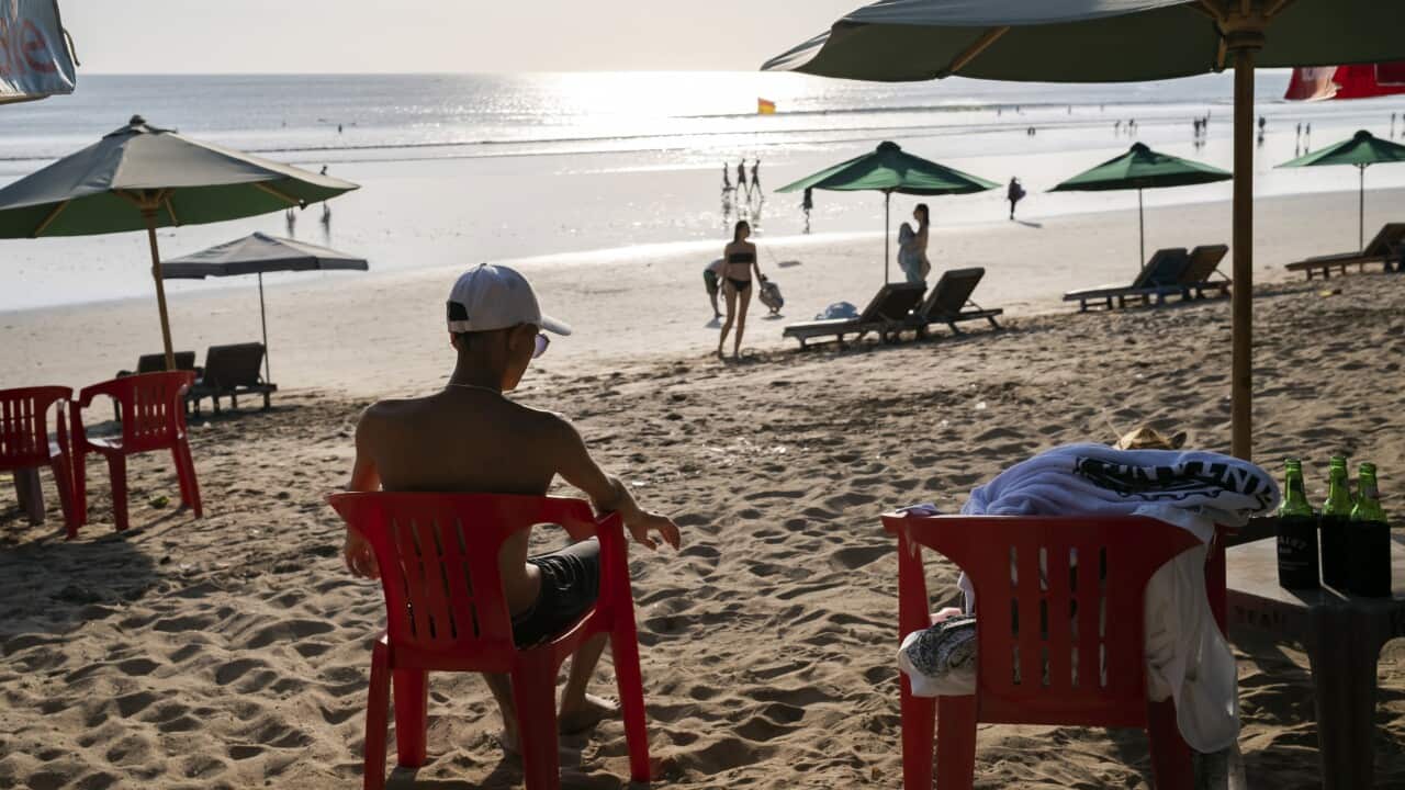 A man sits on a chair on the beach as more tourists are seen closer to the sea.