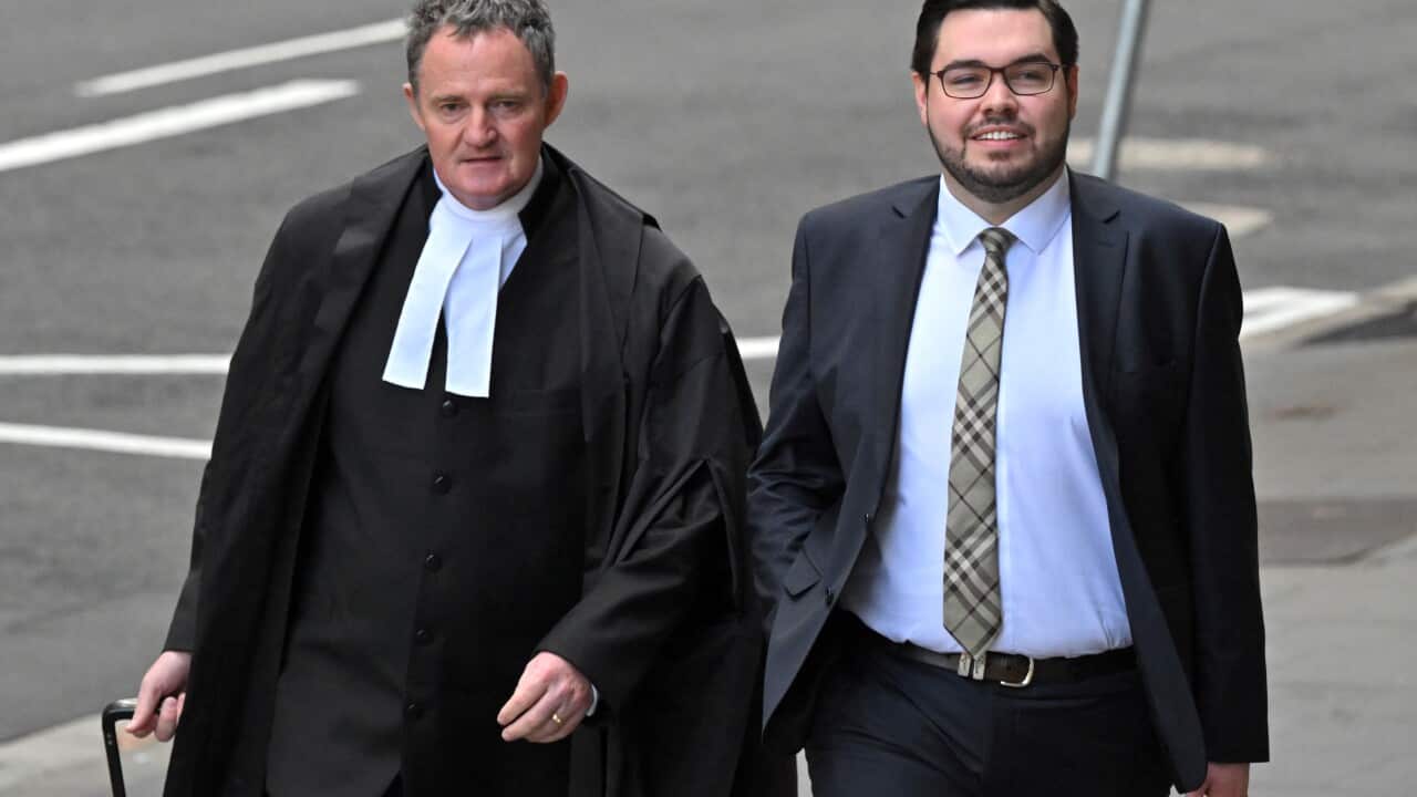 Two men walking down a street. One wears a suit, the other the uniform of a barrister.