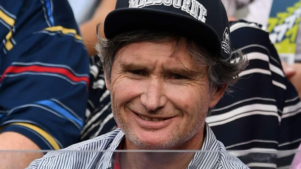 Dave Hughes sitting among people. He is wearing a cap that reads "Melbourne"