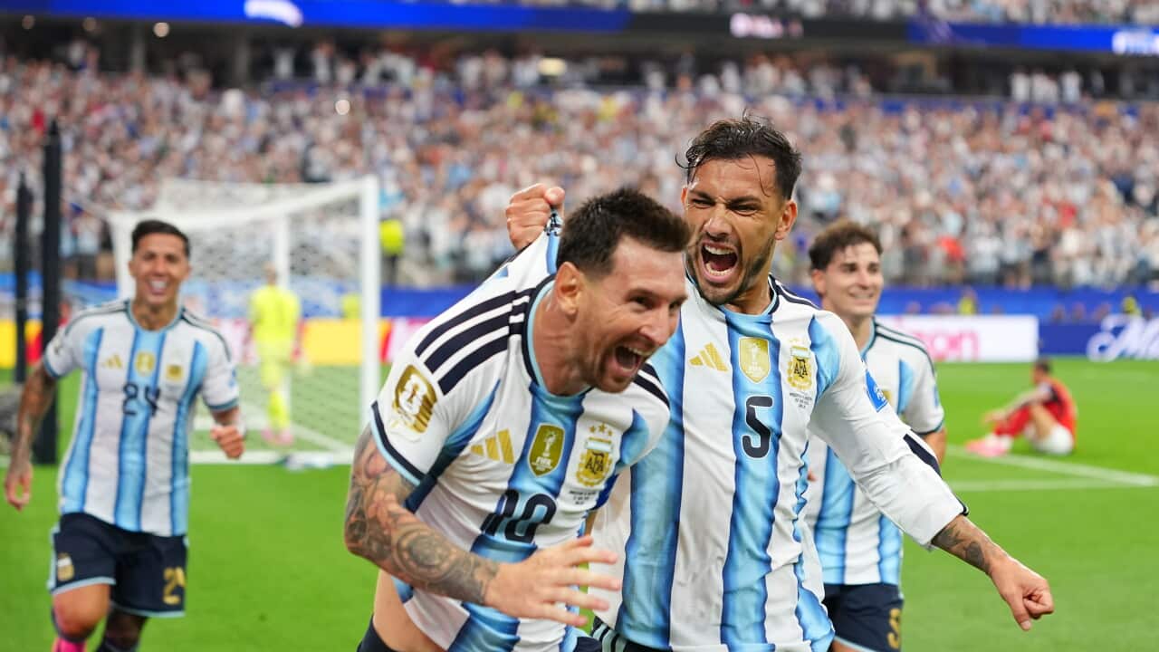 A football player wearing a light blue and white jersey is elated after scoring a goal. His teammate in a light blue and white jersey is pulling his shirt as he also celebrates with him. Two other teammates are seen running behind them, smiling.