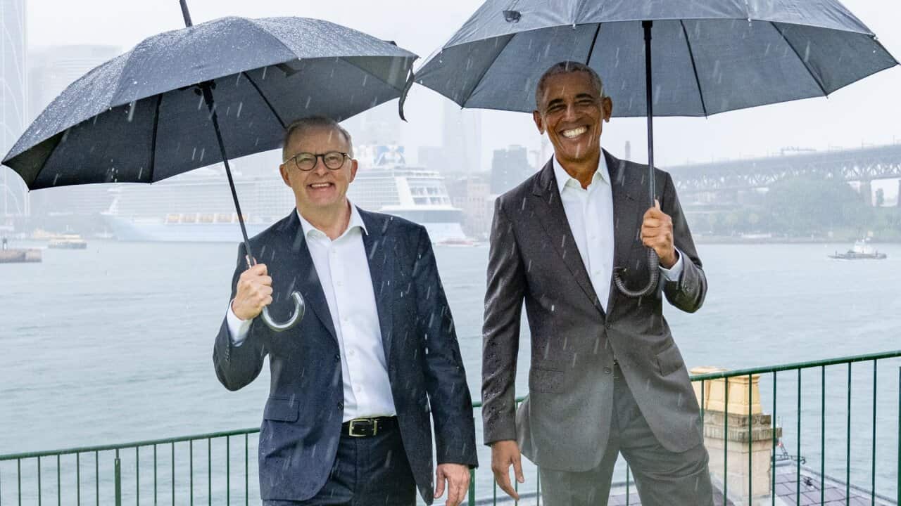 Anthony Albanese and Barrack Obama standing in front of Sydney Harbour, each holding an umbrella over their heads.
