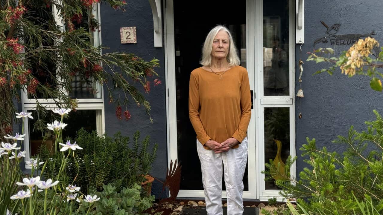 A woman wearing a mustard top and white pants is standing in a garden in front of a unit.