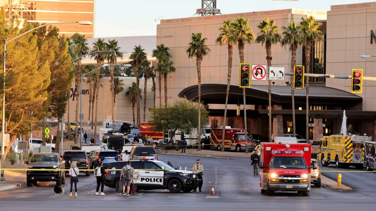 Emergency vehicles and yellow tape blocks of a road in front of a large orange building.