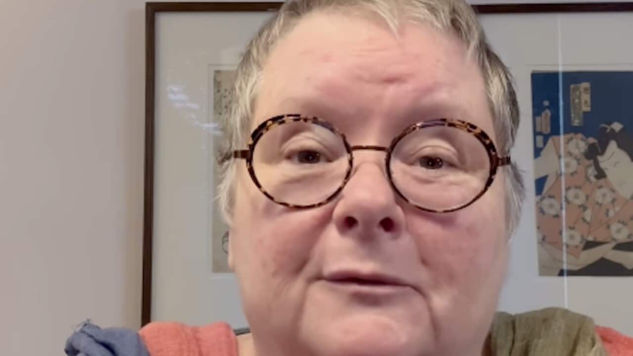 A woman with short grey hair and brown glasses.