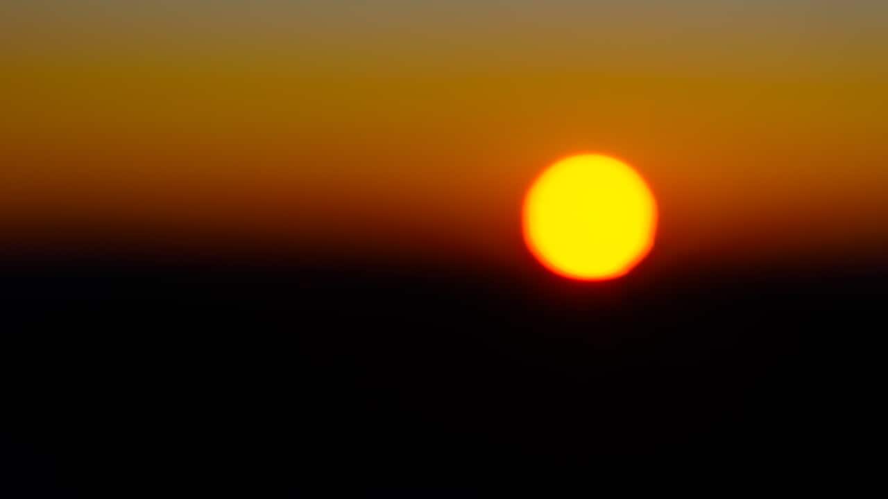 A dramatic contrast of red and black behind the gold disc of the sun.