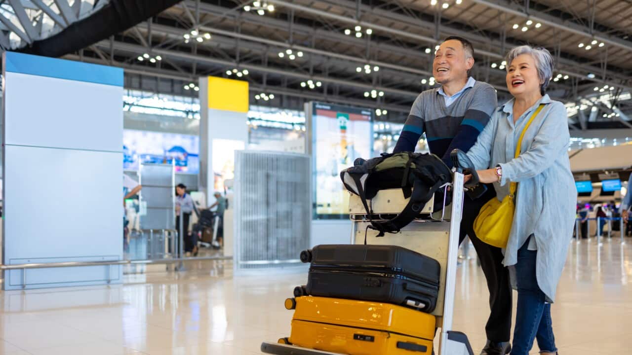 Asian senior couple with luggage trolley walking together in Airport Terminal.