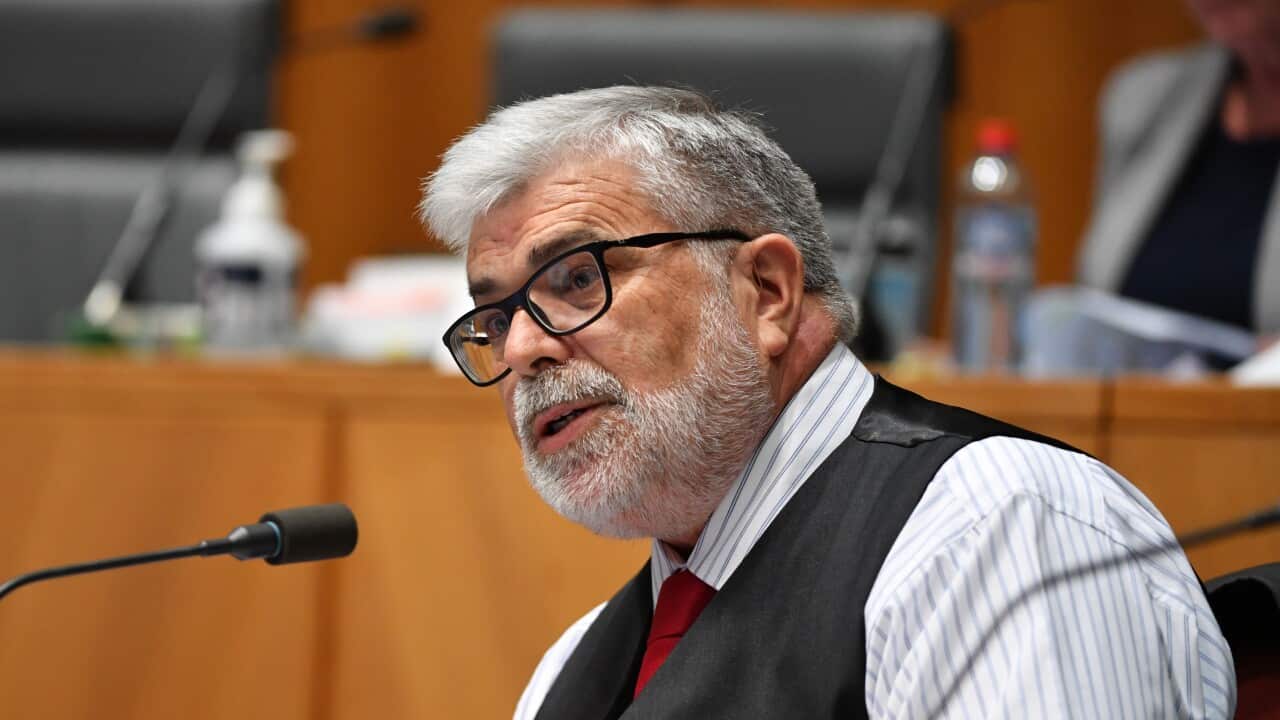 A man in black-rimmed glasses and a black waistcoat sits in front of a microphone.