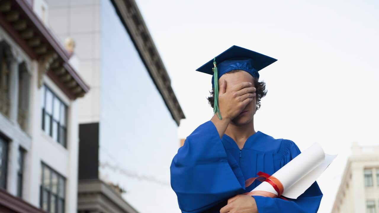 A Graduate In Cap And Gown Holds His Hand Over His Eyes