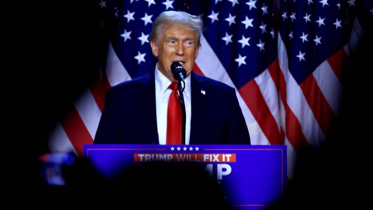 Donald Trump standing in front of the US flag.