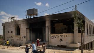 Children are seen standing outside a burned building. Graffiti are scrawled on the building wall in Hebrew.