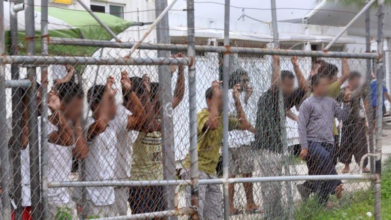 Asylum seekers staring at media from behind a fence at Manus Island