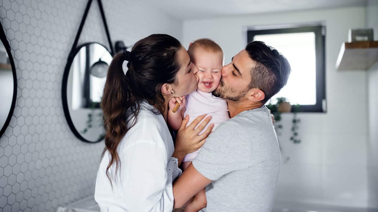Portrait of young couple with toddler girl in the morning indoors in bathroom at home, kissing.