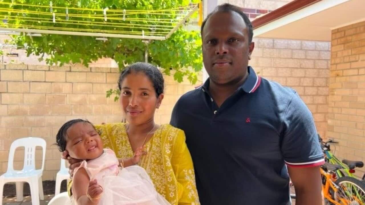 A woman holding a small baby with a man beside her.