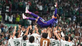 A football team in white shirts lift their goalkeeper, dressed in purple, in celebration.