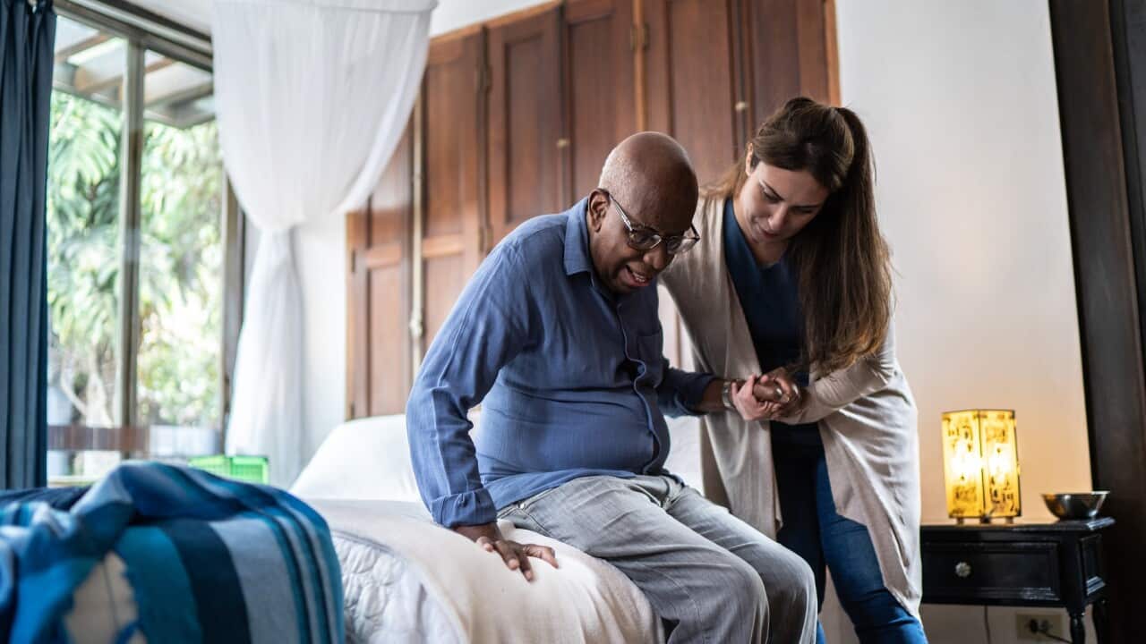 Home caregiver helping a senior man standing up at home