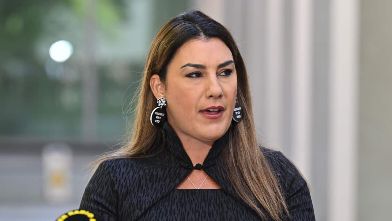 Lidia Thorpe speaks outside. There is a microphone to her right. She is wearing all black, and has earrings which read 'sovereignty never ceded'.