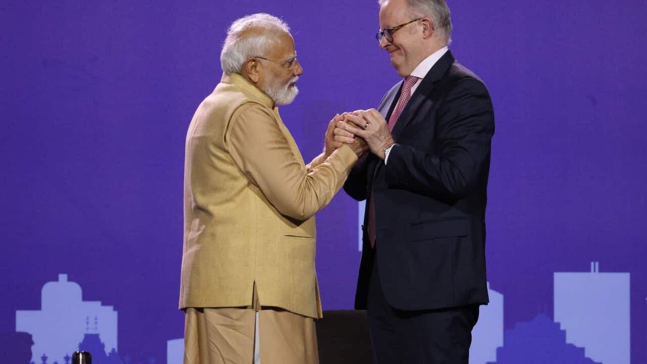 Narendra Modi,Anthony Albanese on stage holding hands in front of a purple background in the stadium.