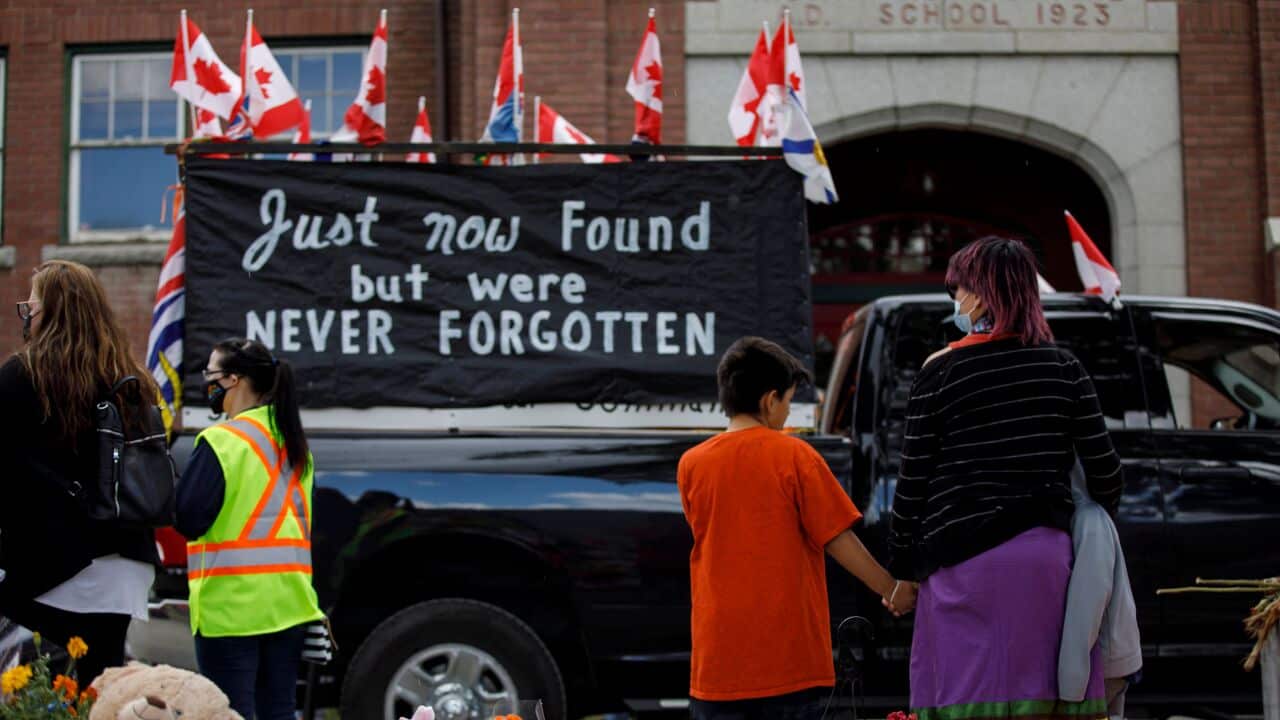People watch as a vehicle convoy passes the former Kamloops Indian Residential School after the remains of 215 children were found near the facility on 5 June.