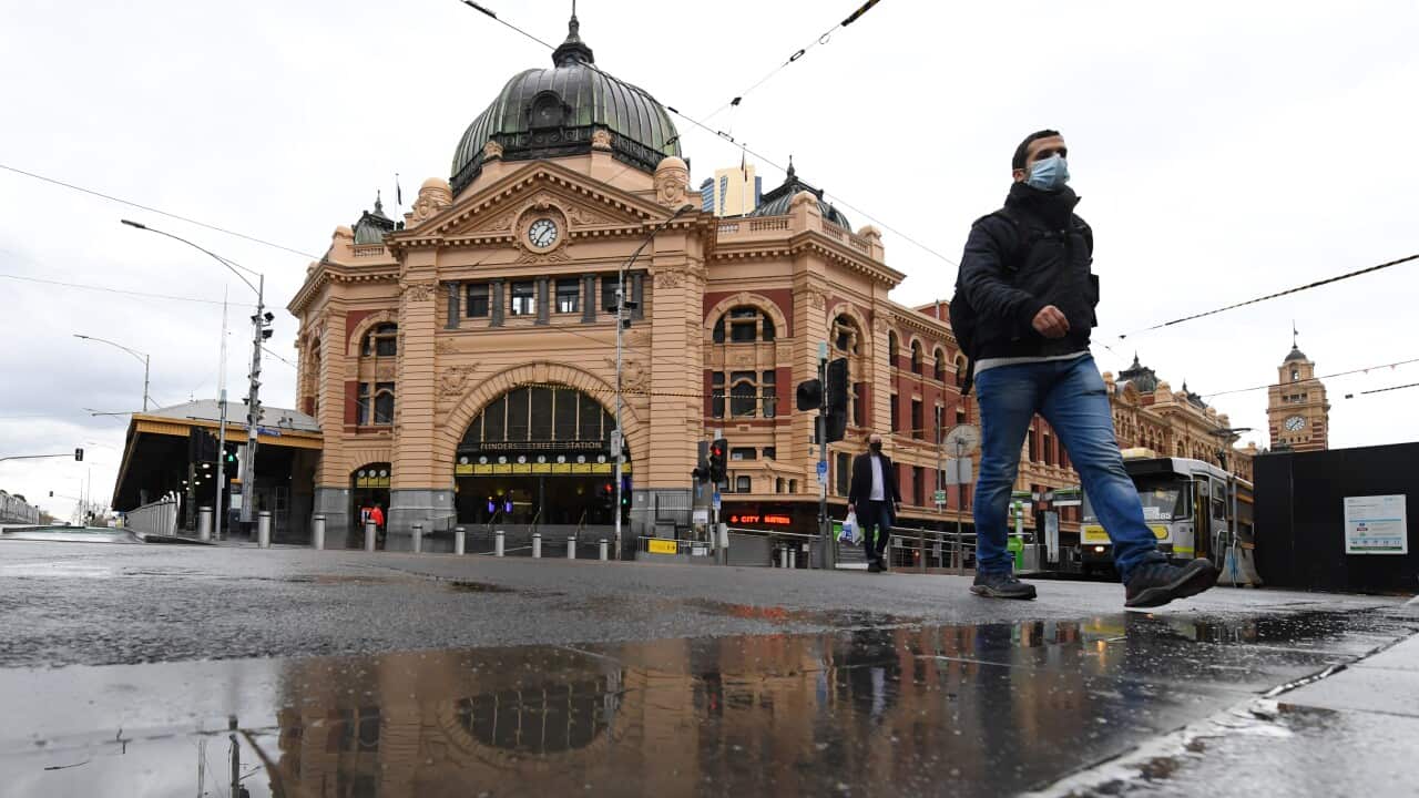 People wearing face masks walk across the road at Flinders Street Station in Melbourne,