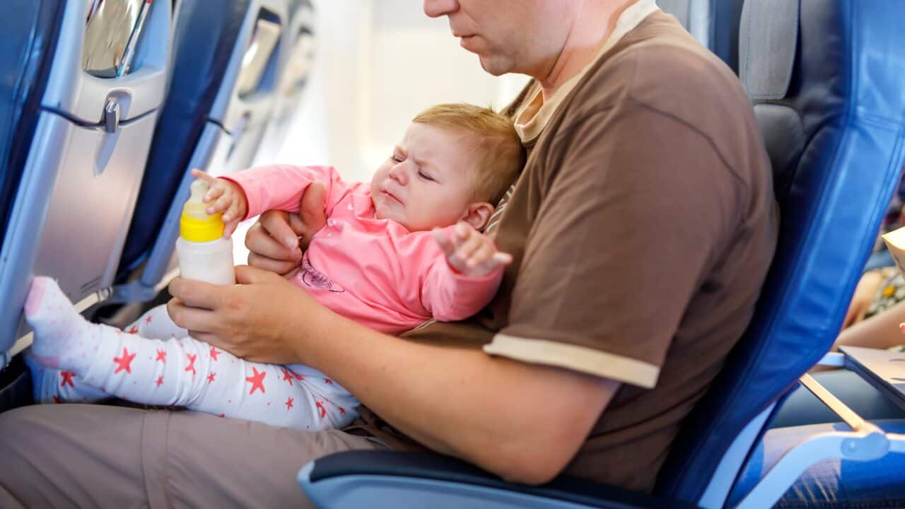 Young tired father and his crying baby daughter during flight on airplane going on vacations