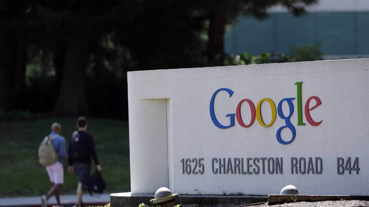people walk past a Google sign at the company's headquarters