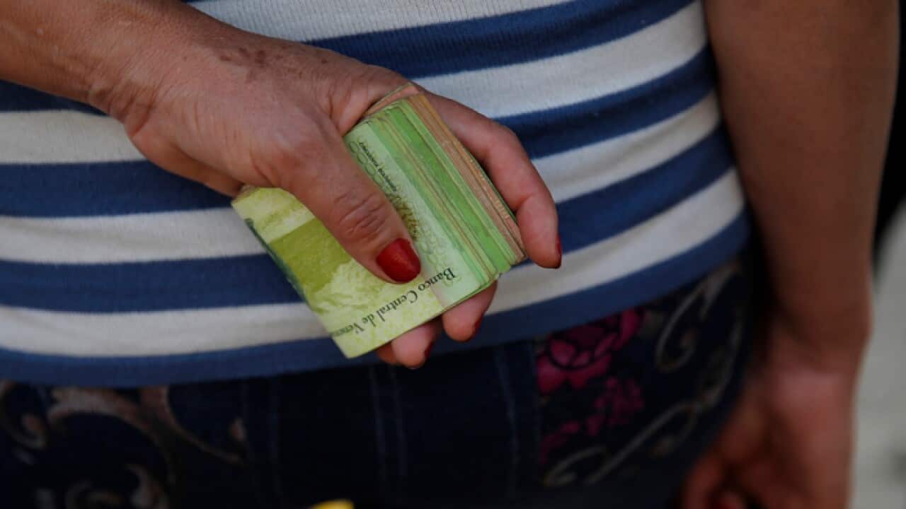 A woman holds a wad of bills to pay her bus fare in Caracas