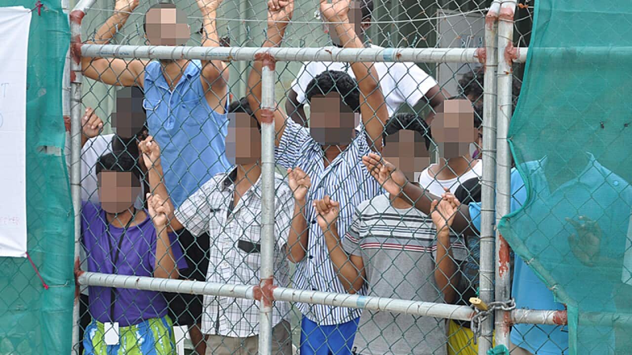 Asylum seekers stare at media from behind a fence.