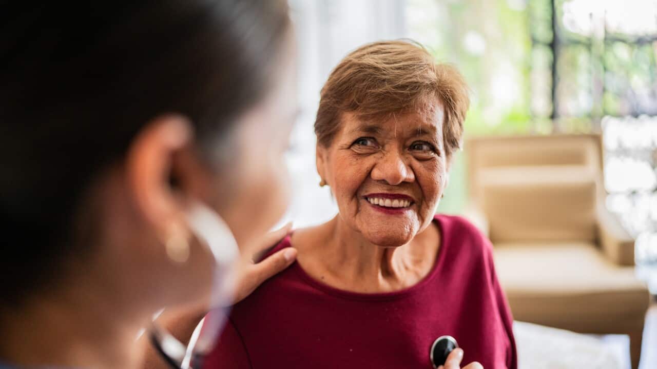 Home caregiver listening to a senior woman's heartbeat in a nursing home