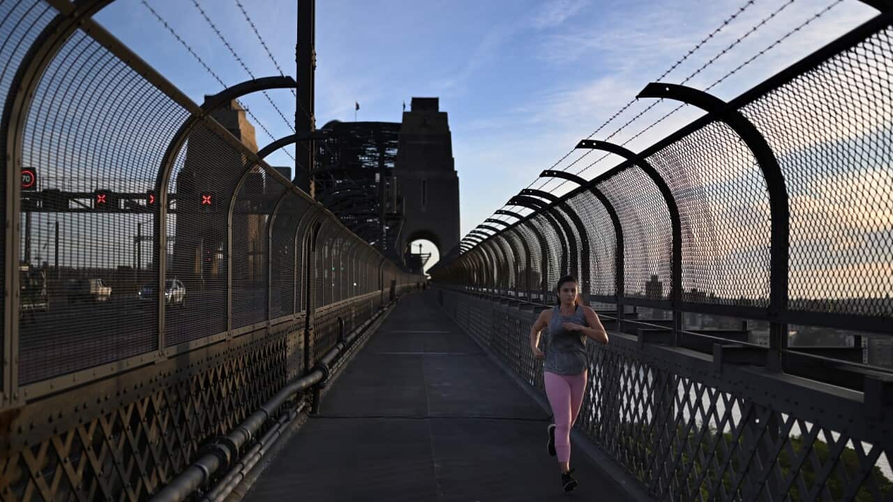 A woman jogs over the Sydney Harbour Bridge at sunrise