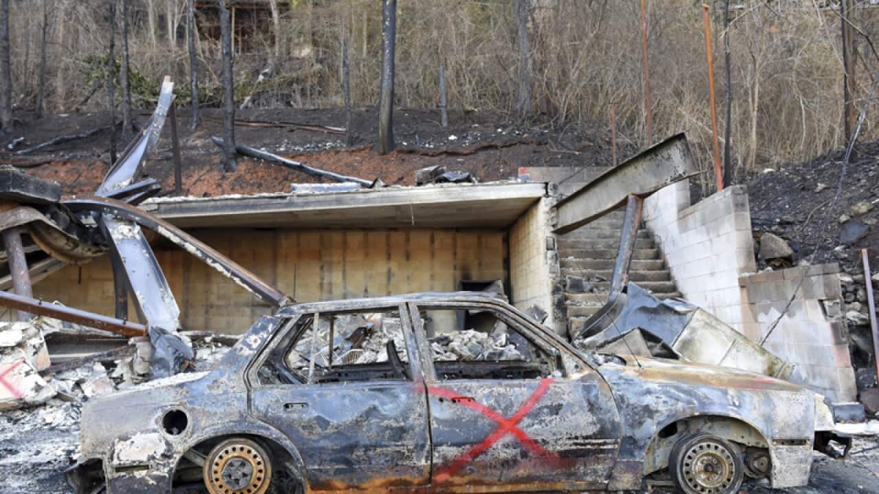A burnt vehicle sits on a wildfire damaged property
