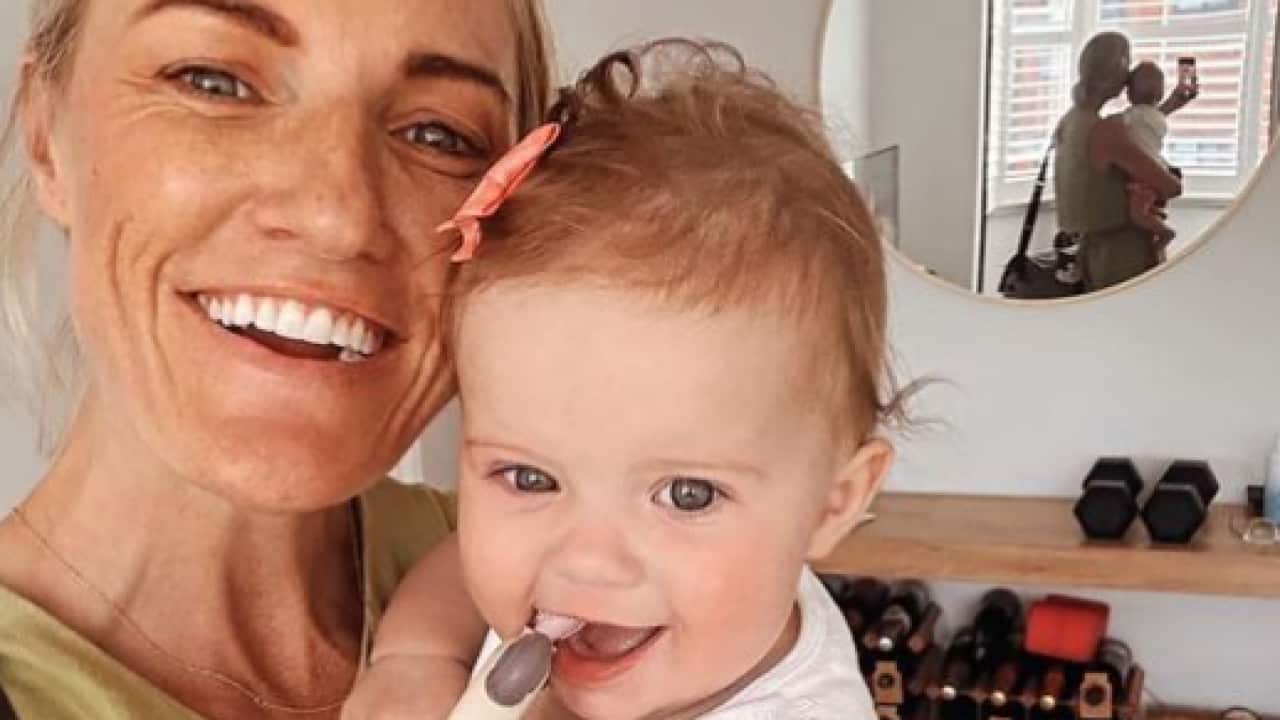 A smiling woman holds a baby in her arms.