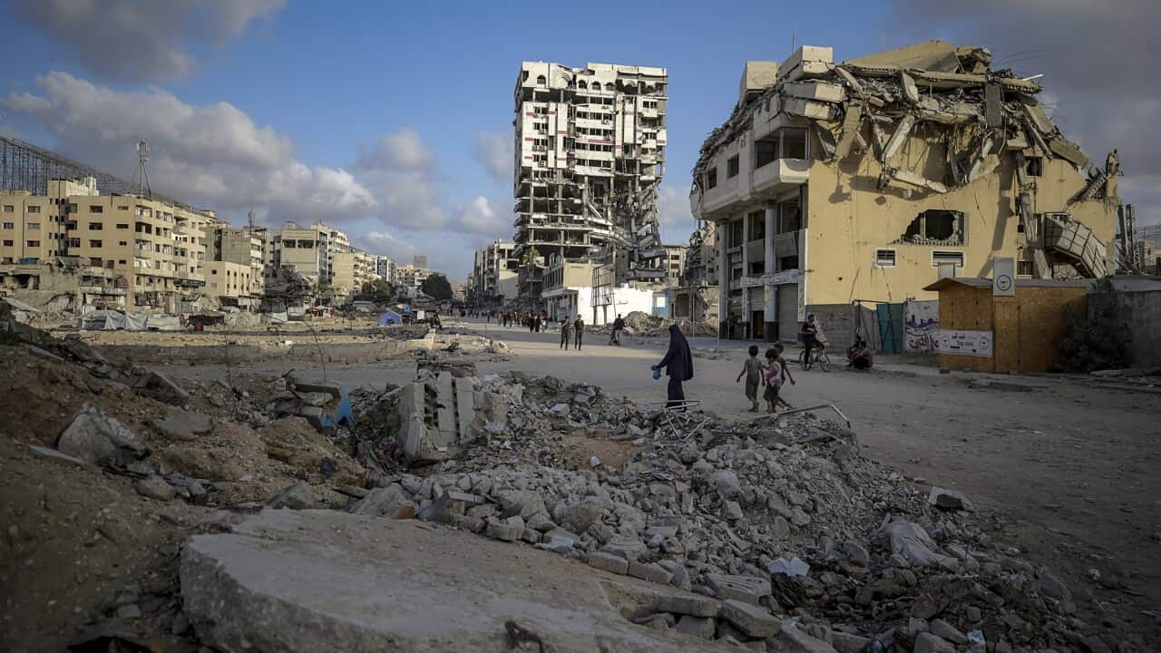 A few residents walk through Gaza City surrounded by building rubble.