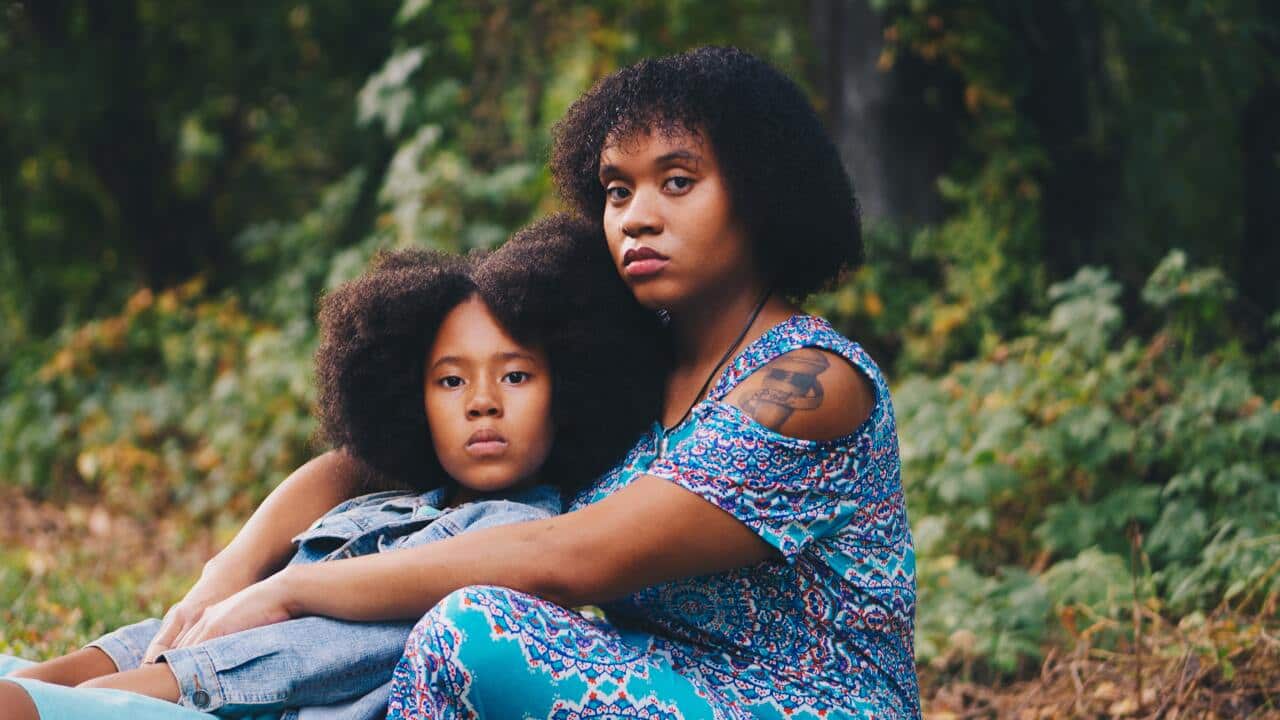 Umwana w'umwigeme ari kumwe na nyina bicaye hasi.