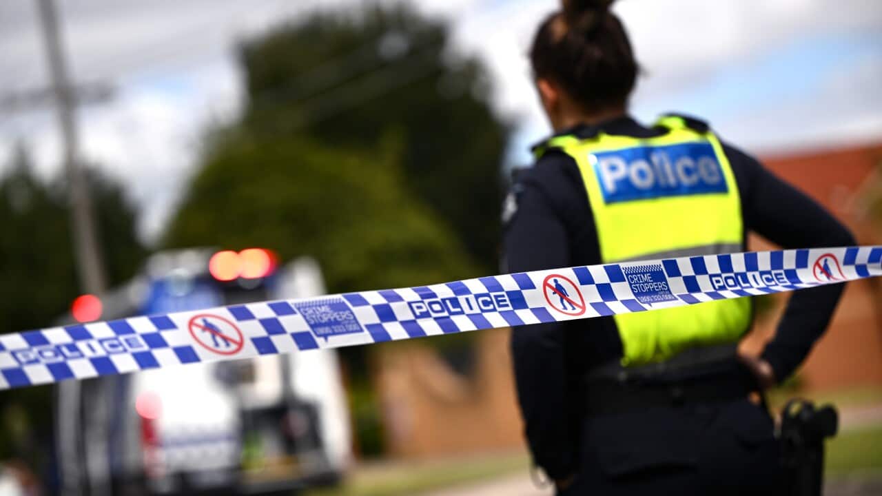 A police officer stands in front of blue and white chequered tape