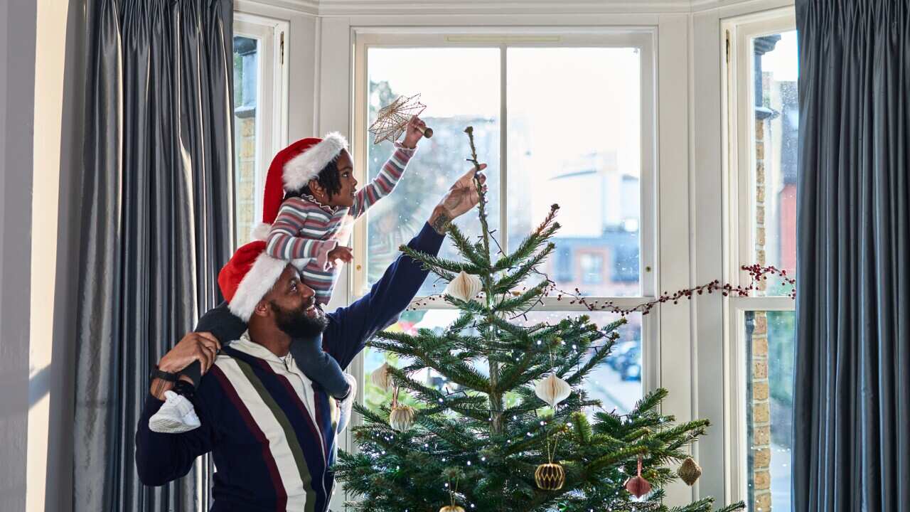 Girl on father's shoulders putting star on top of Christmas tree
