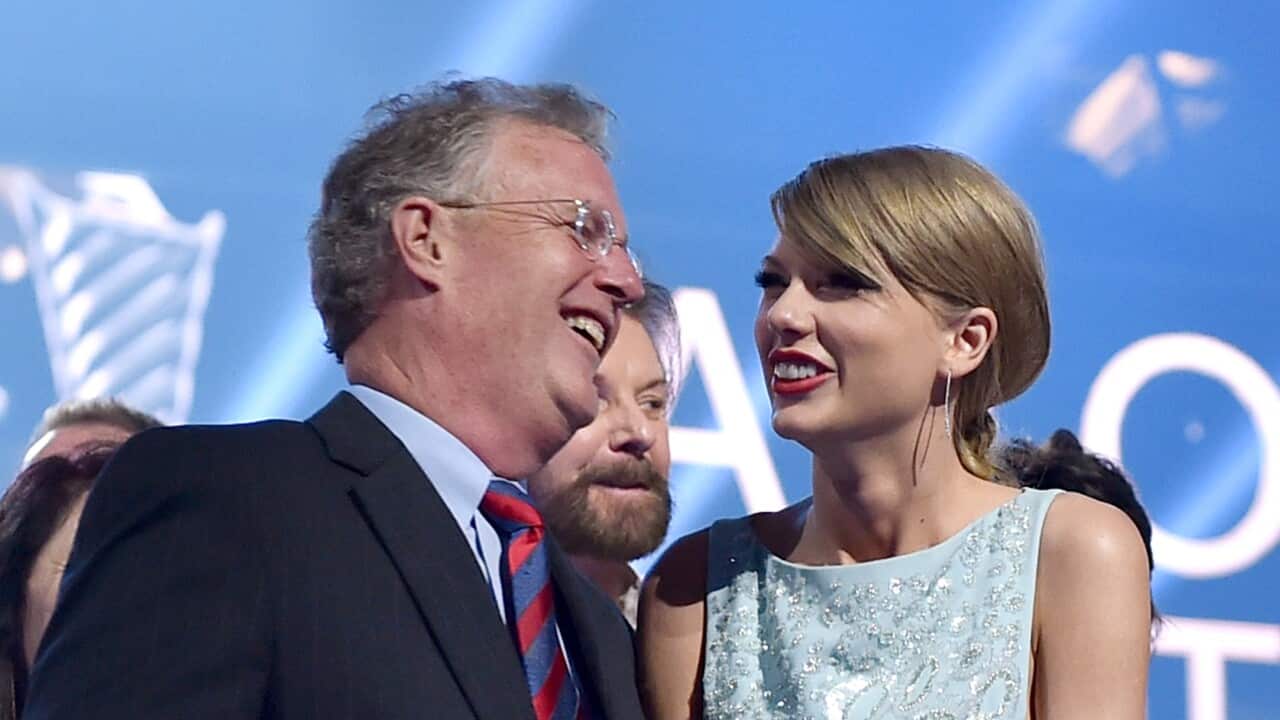 Scott Swift and Taylor Swift smiling at each other in front of a blue background.