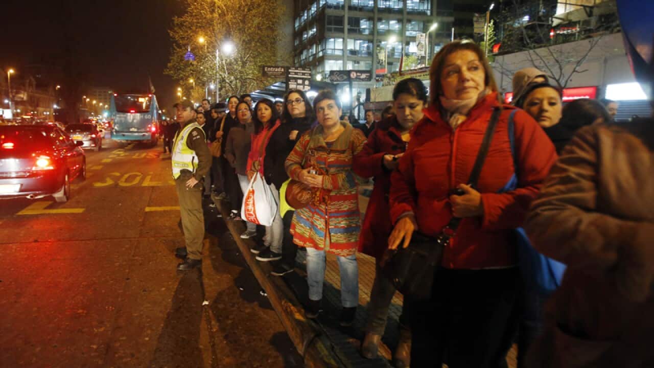 An officer flags down buses for people after an earthquake in Santiago
