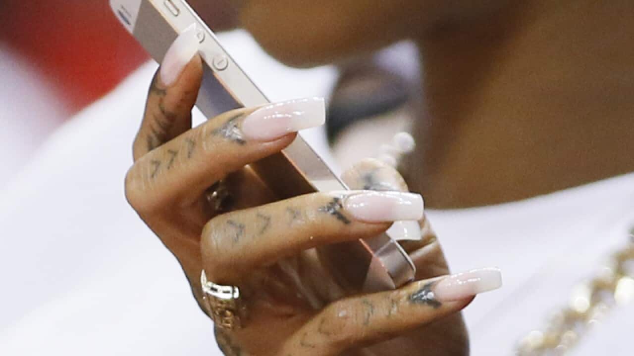 The fingernails of Rihanna are seen as she holds her iPhone