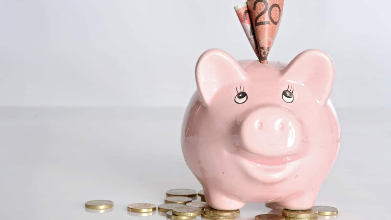Pink piggy bank with an Australian $20 note tucked into the top, surrounded by Australian coins on a white background.